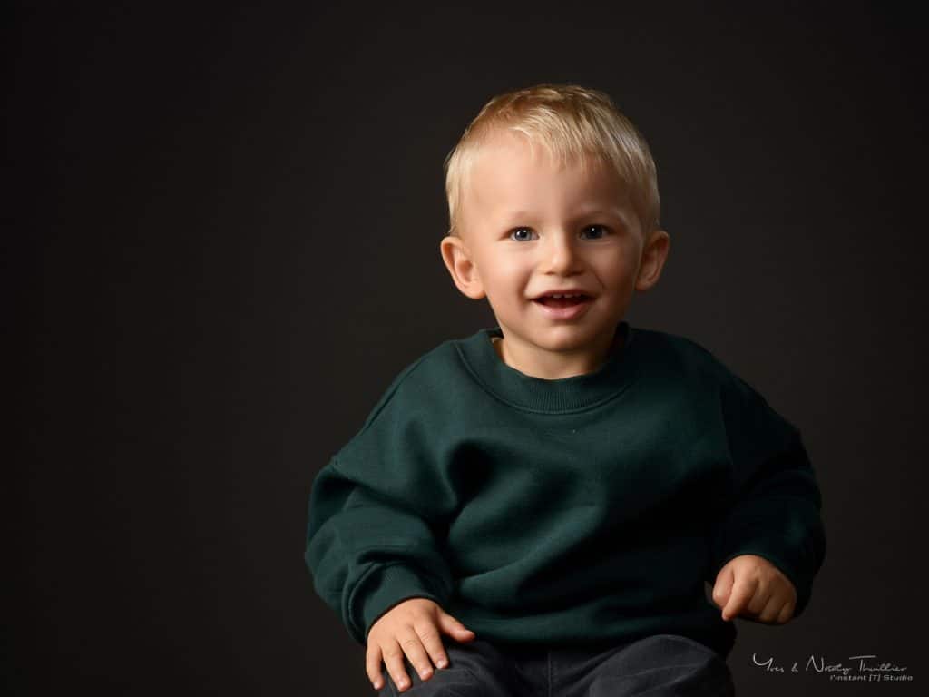 Petit garçon blond souriant en pull vert, séance photo enfant au studio d'Annecy