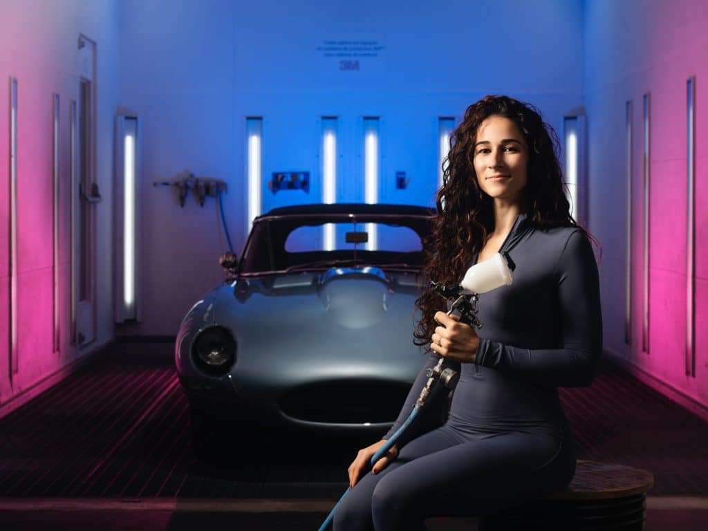 Femme posant devant une voiture de collection en cabine de peinture