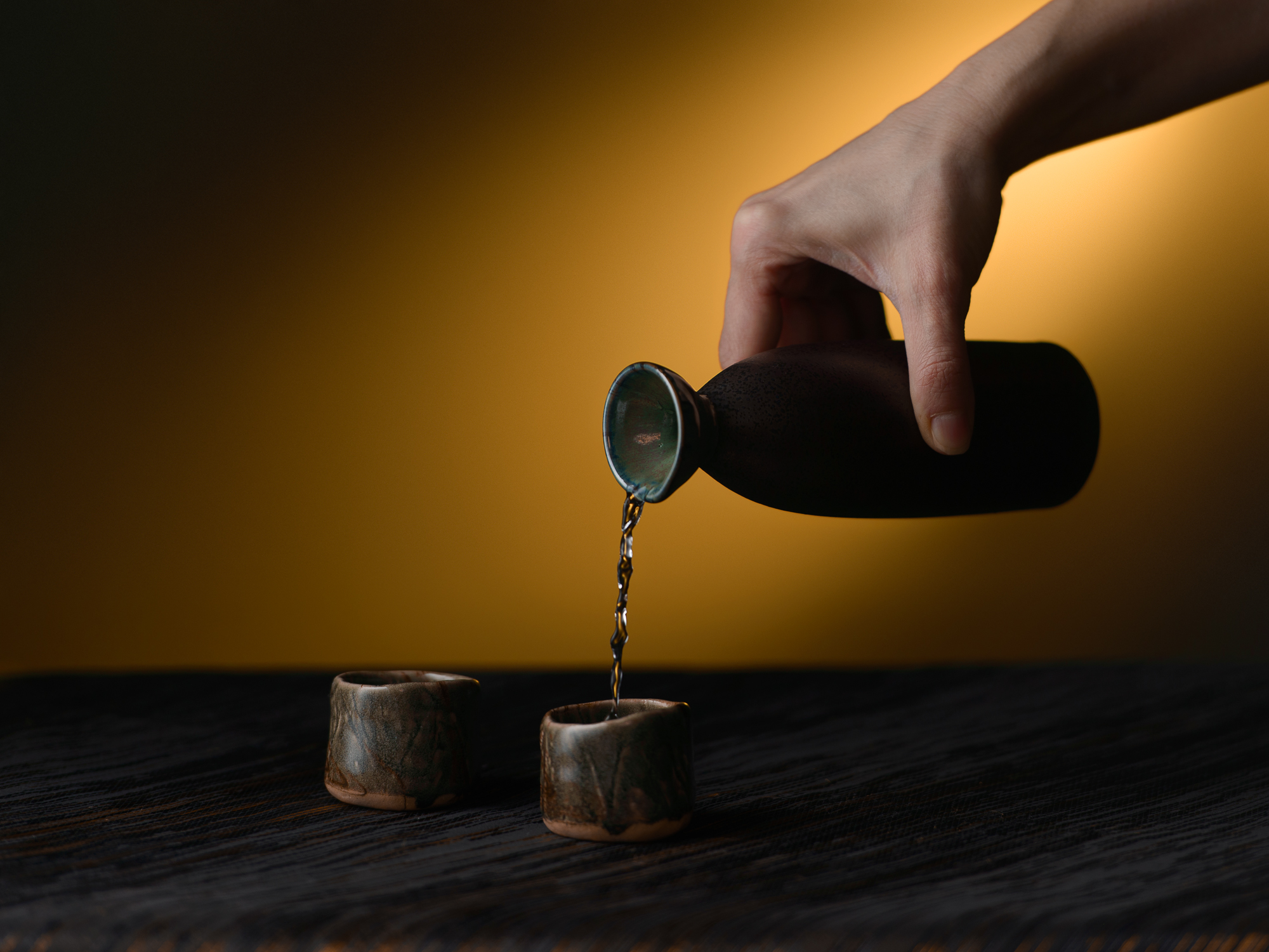 Liquide versé d’une bouteille sombre dans un verre, lumière dorée, photographe produit Annecy