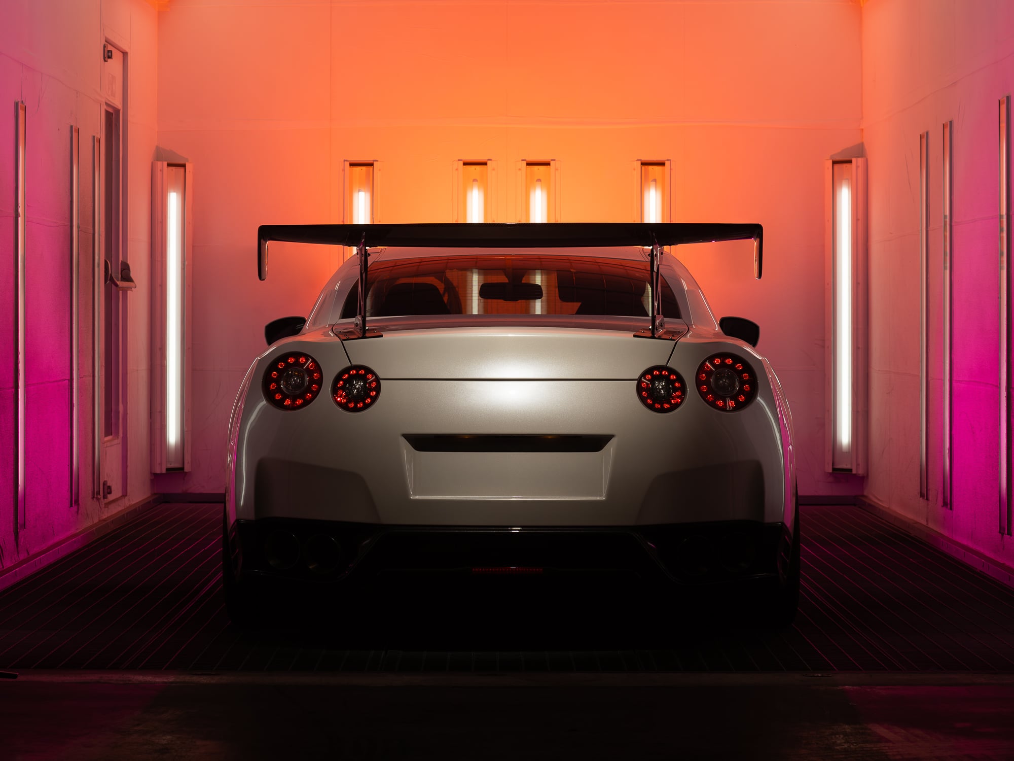 Voiture de sport vue arrière dans une cabine de peinture en lumière orange et rose