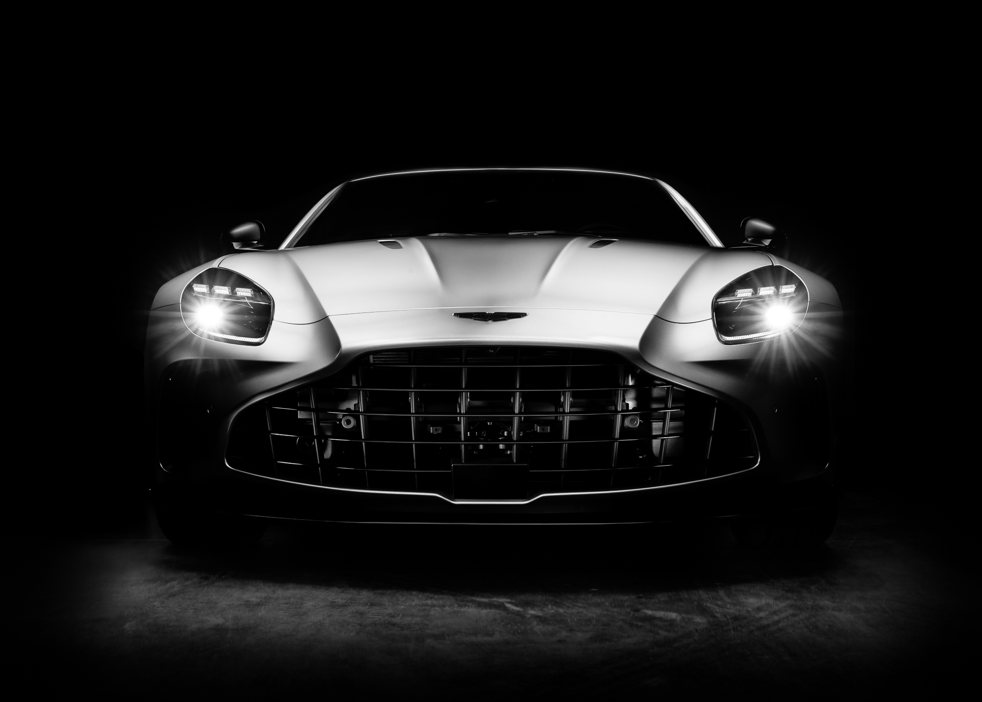 Face avant d’une Aston Martin dans le noir, phares allumés