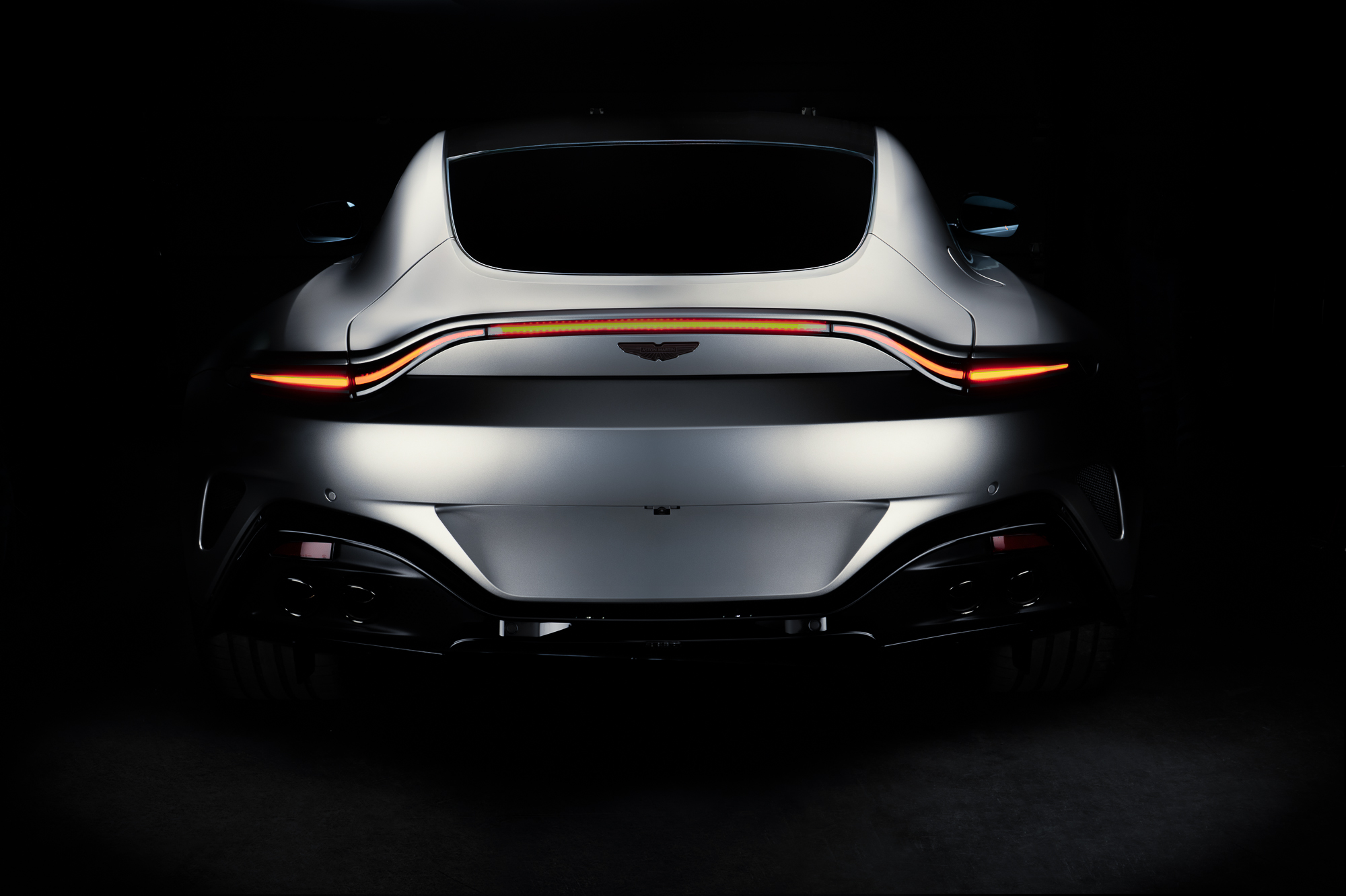 Aston Martin Vantage vue arrière sur fond noir, feux allumés, photo automobile en lumière studio