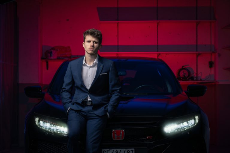Portrait d’un débosseleur devant une voiture, phares allumés, fond rouge