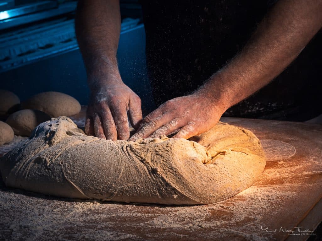 Mains du boulanger travaillant la pâte sur le plan fariné, photographie du geste artisanal